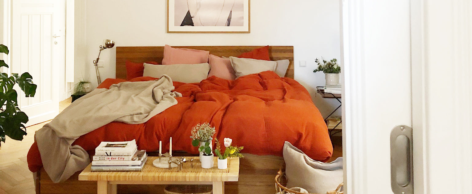 Bedroom in an old building with a modern wooden bed and elegant muslin bed linen from Hutch&Putch in rust red, combined with pillows in stone gray and old pink.